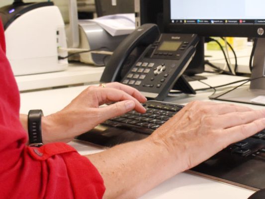 Handen op een toetsenbord naast een telefoon, tijdens het werken aan een administratie