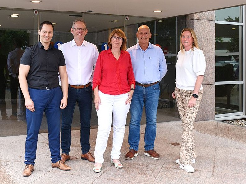 De vijf medewerkers van Schrauwers & Van der Neut staan samen voor de ingang van het kantoor in Badhoevedorp